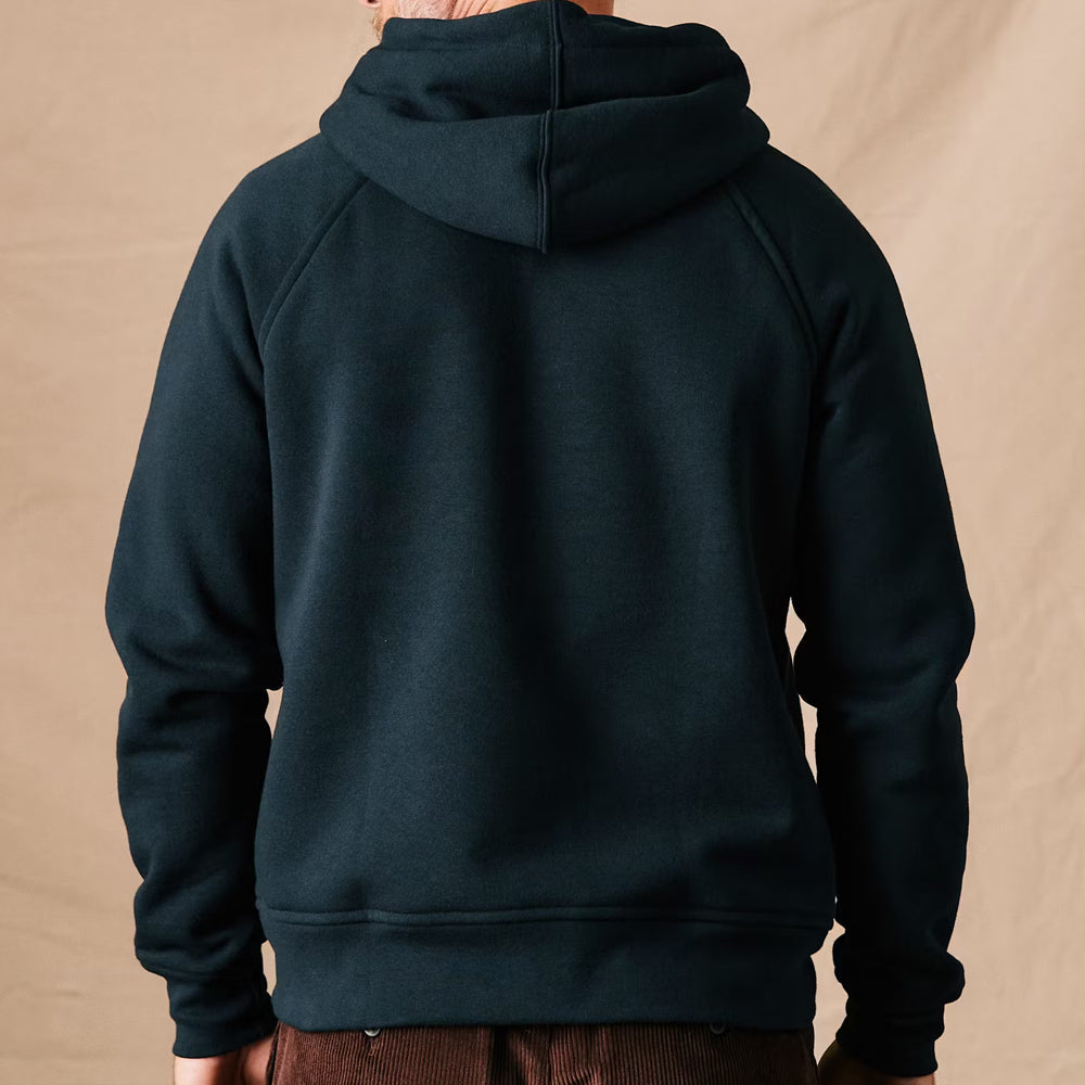 Dark green hoodie worn by a person on a beige background