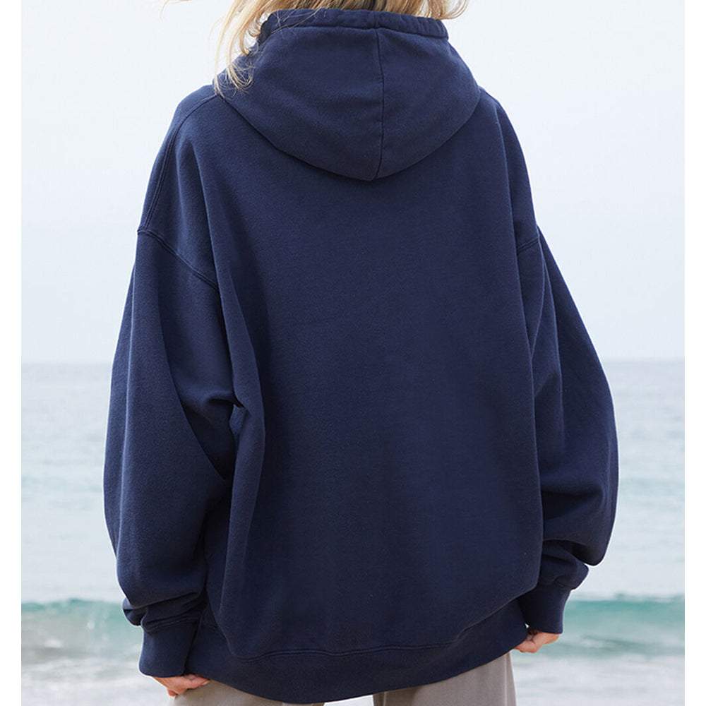 Person wearing a navy blue hoodie with a blurred beach background