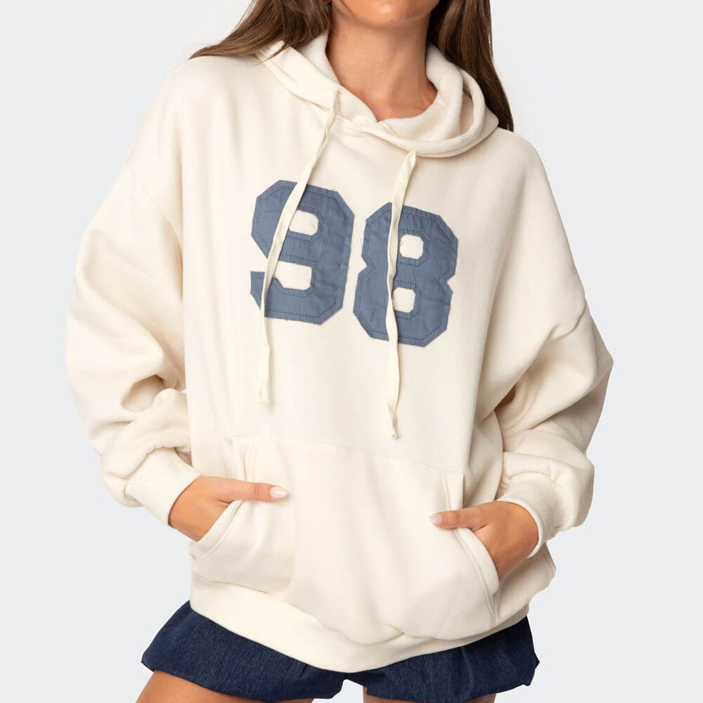 White hoodie with blue '98' design worn by a person on a light gray background