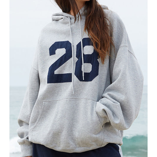 Person wearing a gray hoodie with the number 28 in navy, standing by a body of water.
